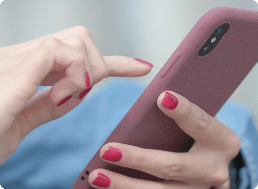 A close-up of a hand with bright red nails tapping on a pink phone case, with a blurred background.