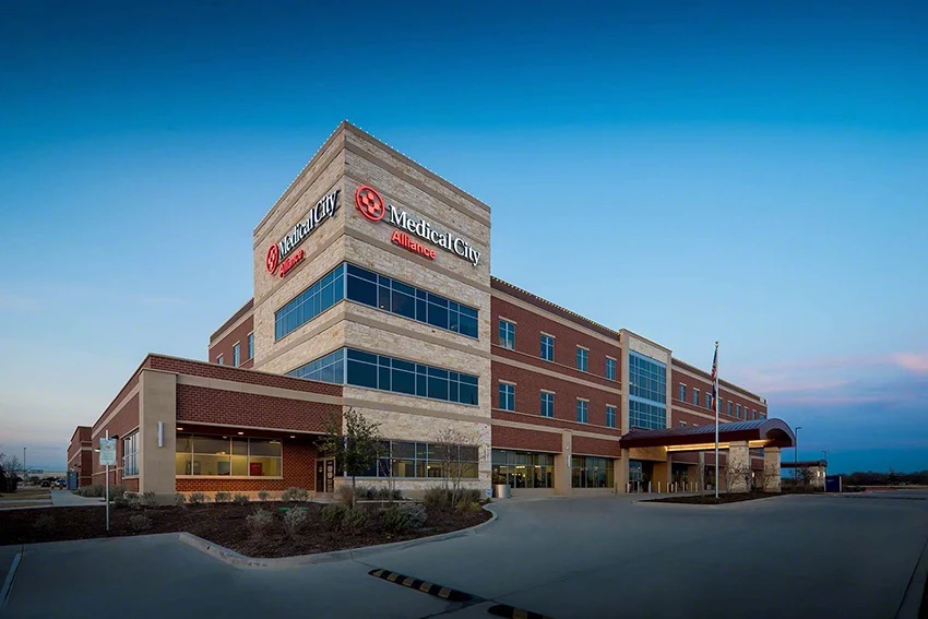 The exterior of Medical City Alliance hospital at dusk, showcasing modern architecture with a welcoming entrance and signage.