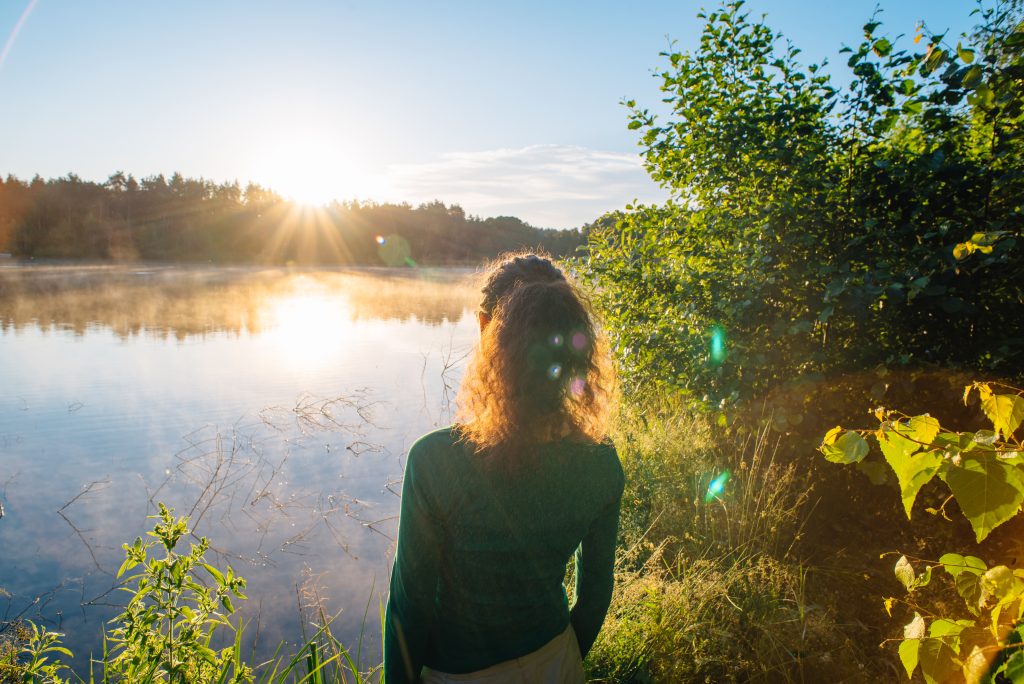 A woman looking at the sun setting across a lake.