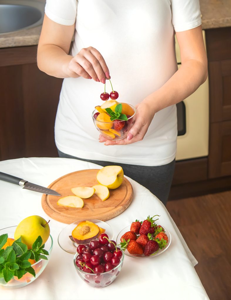 Cropped view of a pregnant woman with bowls of fruit.