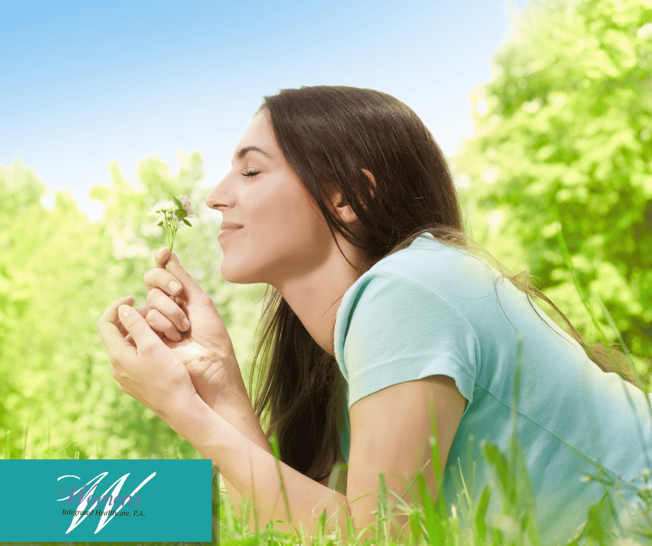 A woman lying in the grass smelling a spring flower.